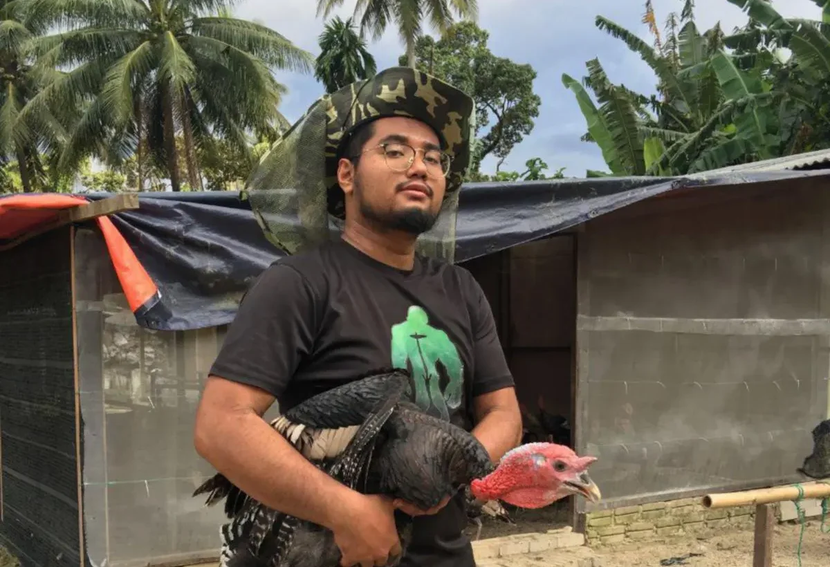 Zainul penternak ayam belanda berdiri di ladang ternakan sambil memegang ayam belanda di Kampung Lalang, Padang Rengas, Perak