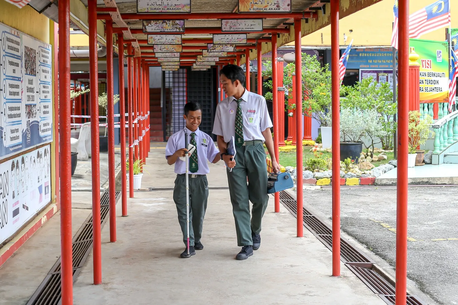 Pelajar OKU penglihatan berjalan di sekolah sambil membawa peralatan Braille.