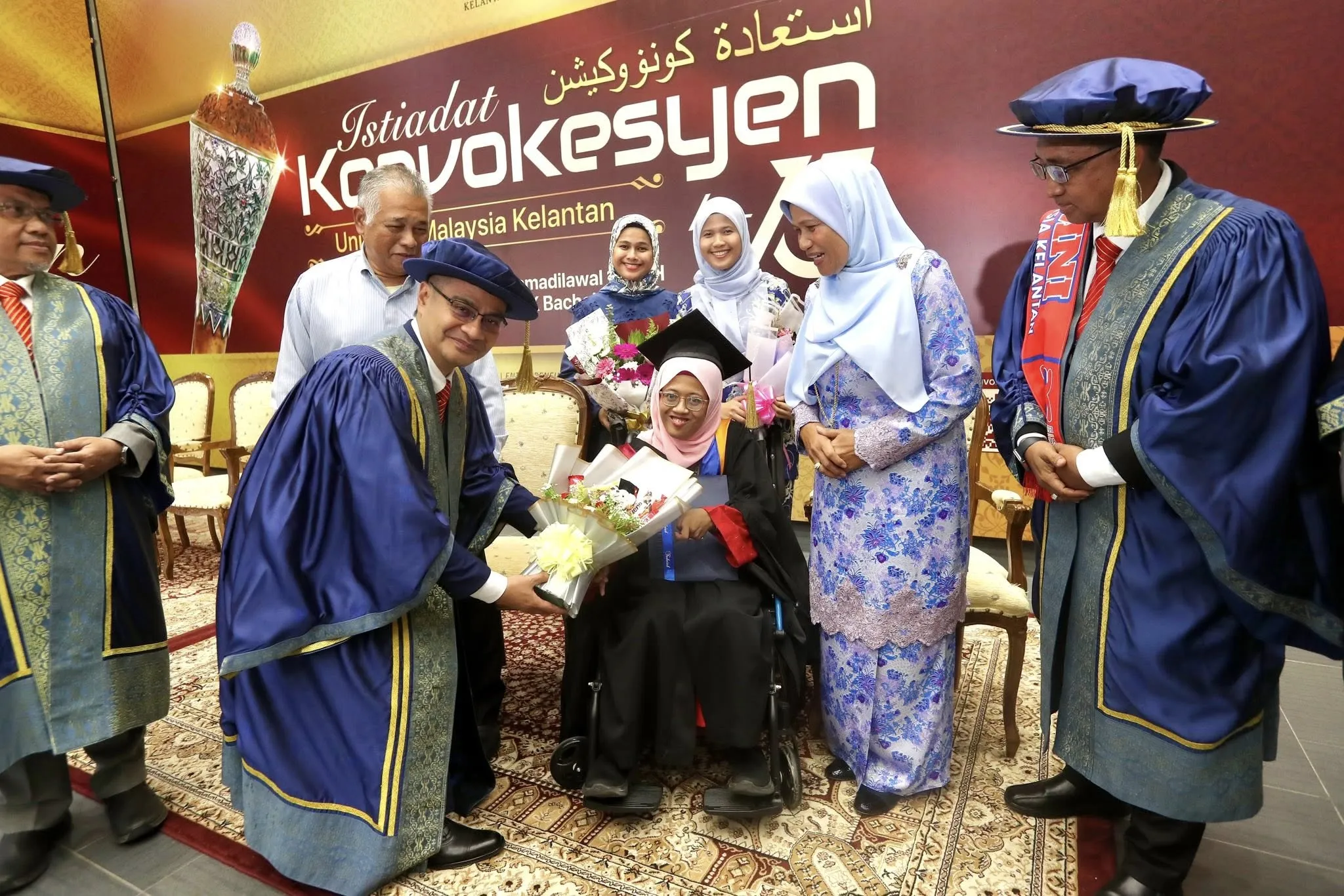 Graduan OKU cerebral palsy menerima skrol di majlis konvokesyen UMK sambil duduk di kerusi roda.