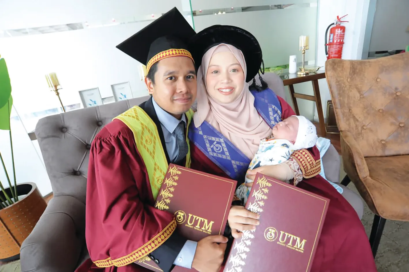 Pasangan graduan UTM memakai jubah konvokesyen bersama bayi semasa majlis graduasi.