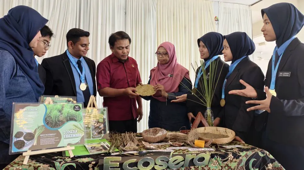 Pelajar dan guru menerangkan produk pinggan serai semasa pameran inovasi Ecosera.