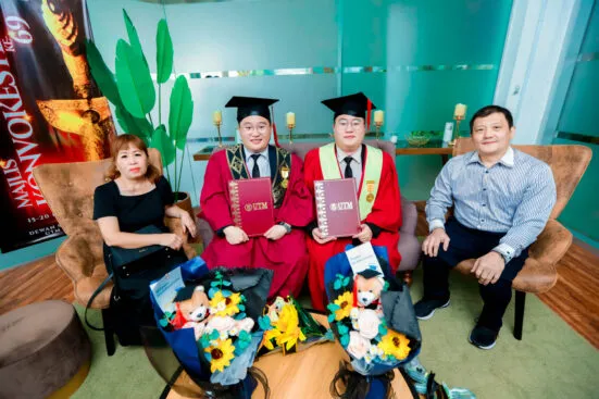 Sepasang graduan kembar UTM bergambar bersama keluarga sambil memegang skrol konvokesyen dan jambangan bunga.
