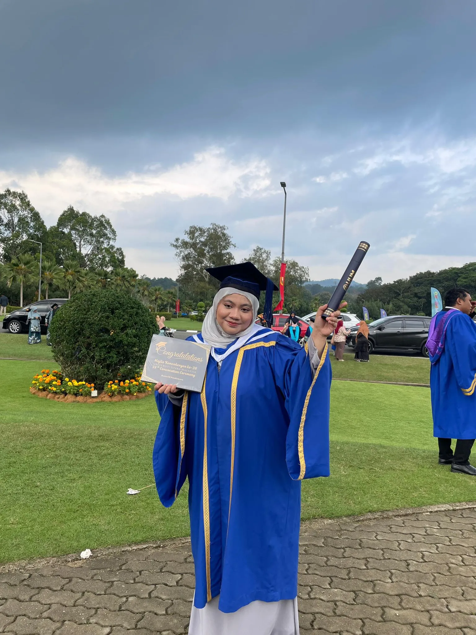 “Graduan wanita memegang skrol dan plak ucapan tahniah semasa majlis konvokesyen.