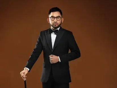 Elrah Azman memakai tuxedo hitam bergaya formal memegang tongkat di studio