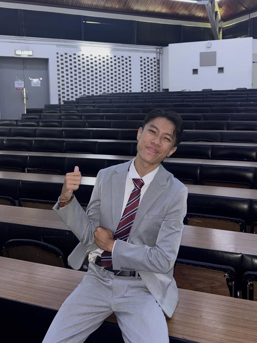 Adib Fahim duduk di dewan kuliah memakai suit sambil menunjukkan isyarat thumbs up sebagai content creator edukasi Matematik