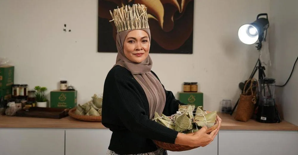 Mama Cah Bak Chang Halal founder posing confidently in her kitchen with packaged products in the background