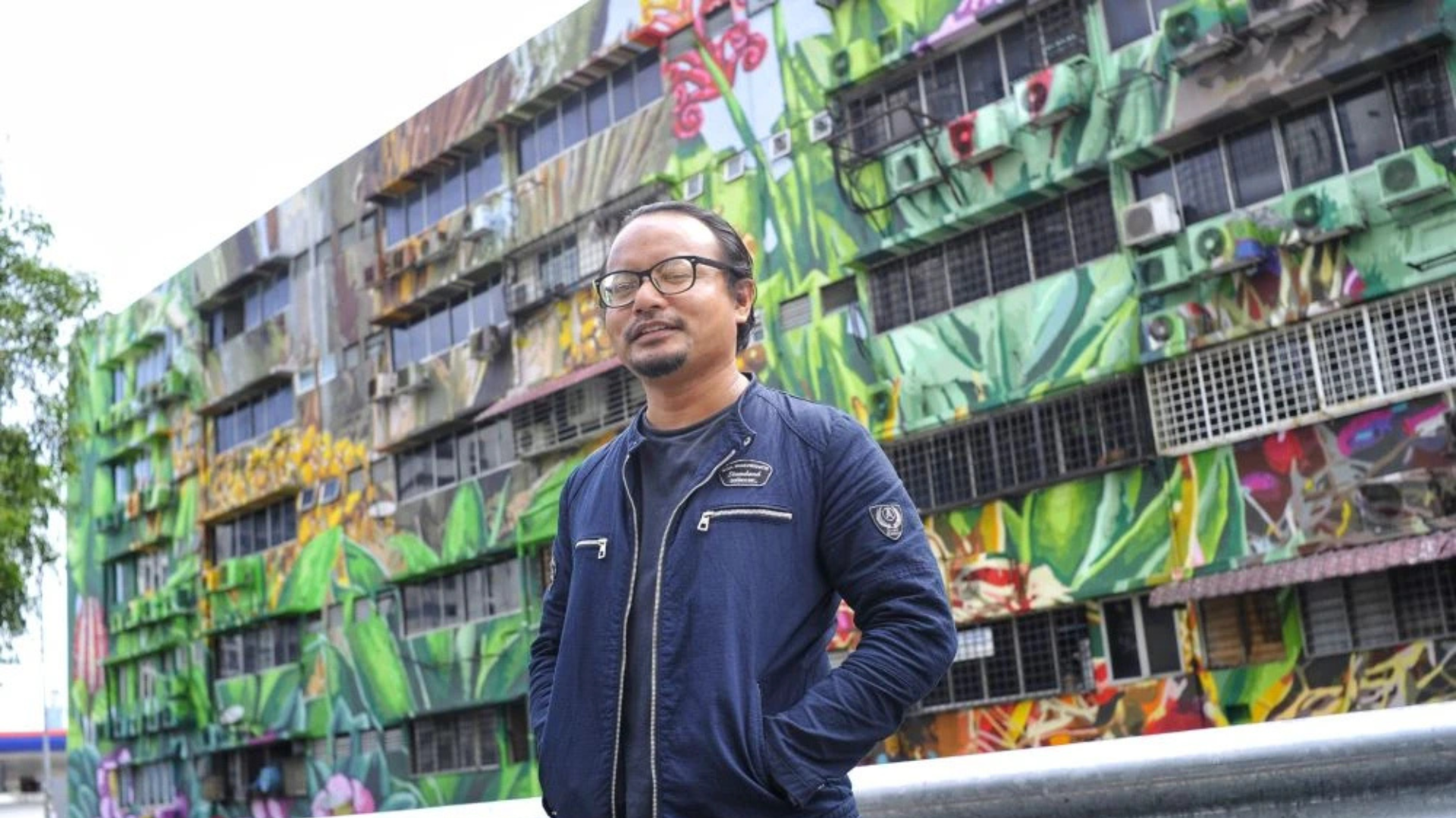 Pak Lan (Fadzlan Rizan Johani), artis mural Malaysia bergambar di hadapan mural berskala besar hasil karya seni bandar di Kuala Lumpur